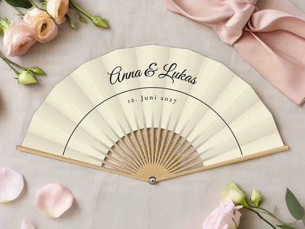 Personalisierter Hochzeitsfächer „Feine Linie“ mit den Namen Anna & Lukas, eine feine Linie im Bogen unter dem Schriftzug, Stoff in Elfenbein mit Druck in Schwarz, auf einem Hochzeitstisch