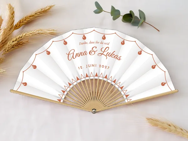 Personalisierter Hochzeitsfächer „Gartenparty“ mit den Namen Anna & Lukas, Lichterkette entlang des Randes und Wimpelfries unten, Stoff in Weiß mit Druck in Terrakotta, auf einem Hochzeitstisch