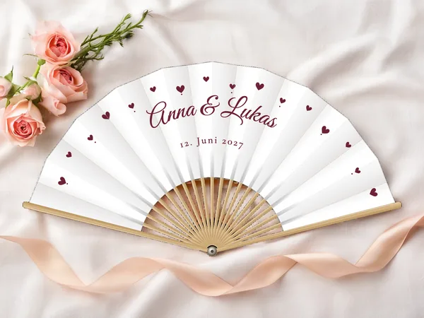 Personalisierter Hochzeitsfächer „Herzen“ mit den Namen Anna & Lukas, kleine Herzen rund um den Schriftzug verstreut, Stoff in Weiß mit Druck in Bordeaux, auf einem Hochzeitstisch