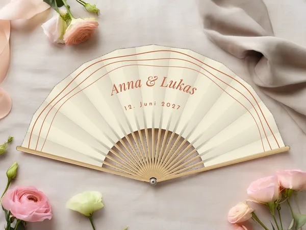 Personalisierter Hochzeitsfächer „Retro-Wellen“ mit den Namen Anna & Lukas, drei parallele Wellenbögen entlang des Randes über dem Schriftzug, Stoff in Elfenbein mit Druck in Terrakotta, auf einem Hochzeitstisch
