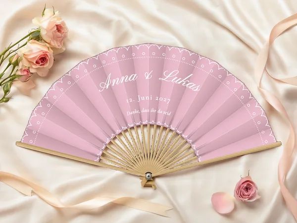 Personalisierter Hochzeitsfächer „Spitze“ mit den Namen Anna & Lukas, gebogte Spitzenkante und Punktlinie entlang des Randes, Stoff in Puderrosa mit Druck in Weiß, auf einem Hochzeitstisch