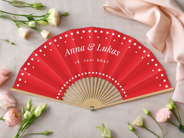 Personalisierter Hochzeitsfächer „Tupfen“ mit den Namen Anna & Lukas, Tupfenreihen entlang des Randes und um die Mitte, Stoff in Rot mit Druck in Weiß, auf einem Hochzeitstisch